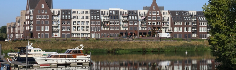 Een rivier met boten op de voorgrond en een woonwijk op de achtergrond.